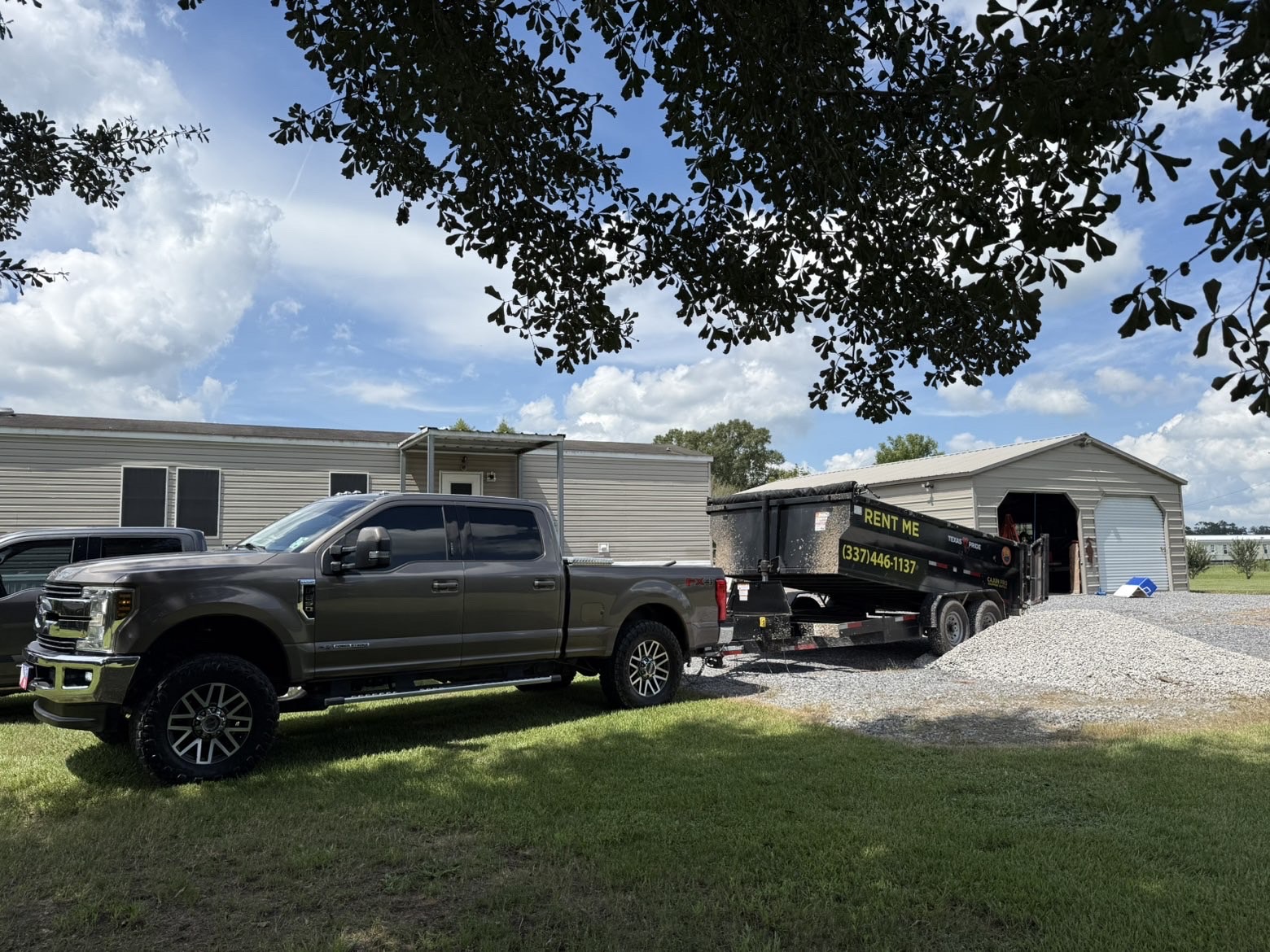 Truck and loaded Rent Me dump trailer parked on a gravel drive