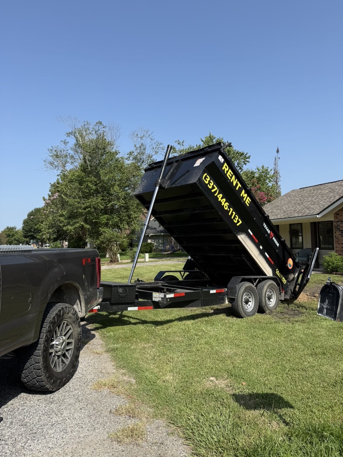 Dump trailer raised and unloading beside a home