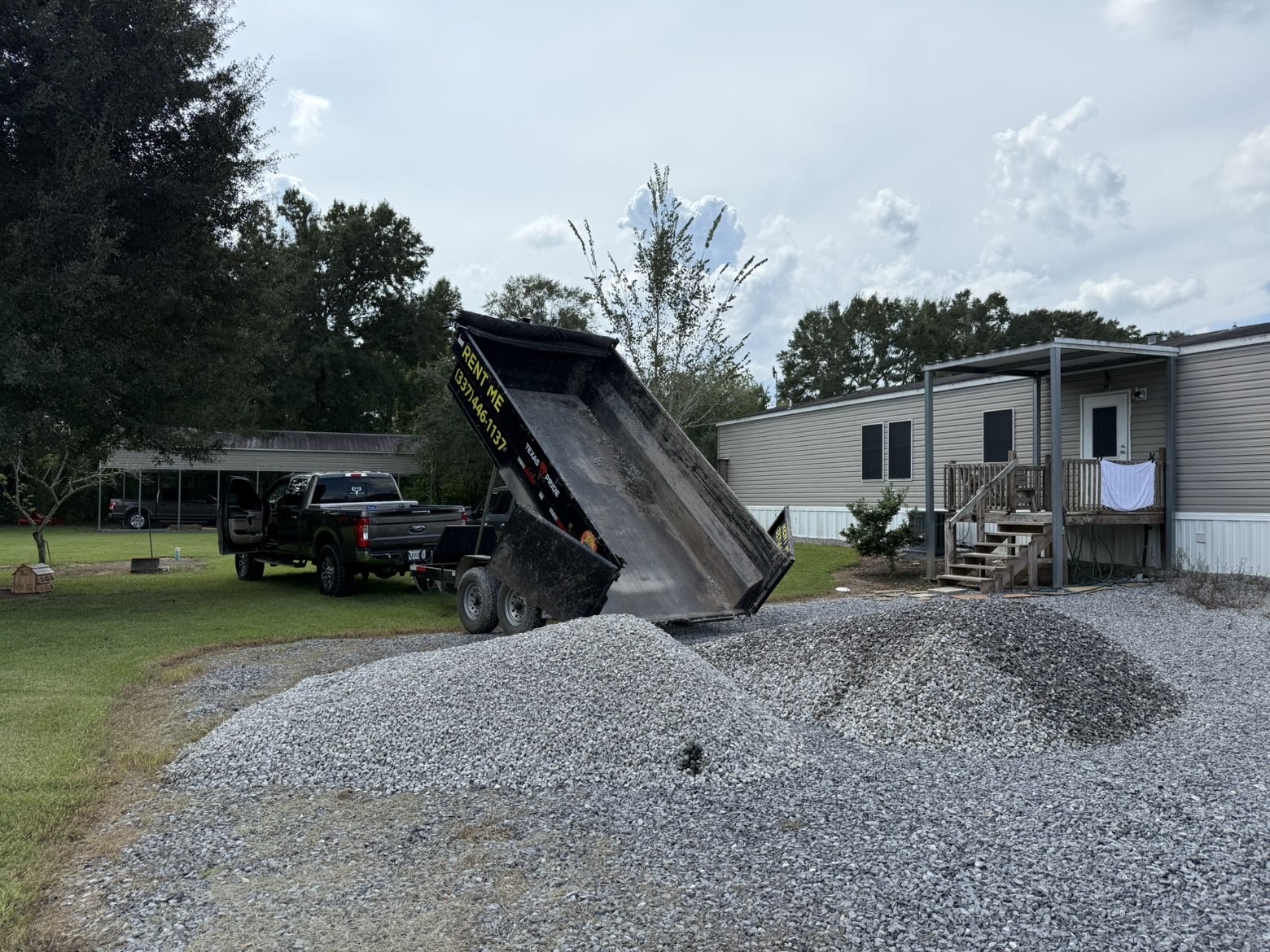 Dump trailer unloading gravel in front of a home